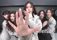 a group of young women standing next to each other in front of a wall holding their hands up