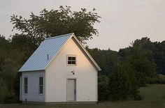 a small white house sitting in the middle of a field next to trees and grass