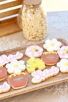 decorated cookies sitting on top of a wooden platter next to a jar of popcorn