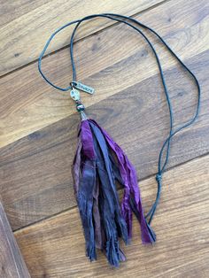 a purple and black tasseled necklace on a wooden floor with a metal hook