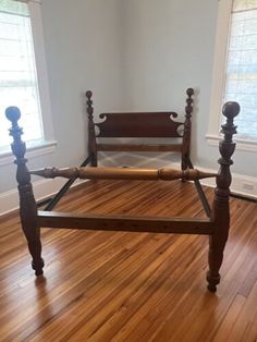 a wooden bed frame sitting on top of a hard wood floor next to two windows