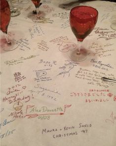 several wine glasses sitting on top of a table covered in handwritten names and phrases