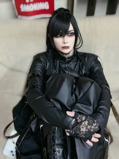 a woman with black hair and leather clothes is posing for the camera while holding her hand on her chest