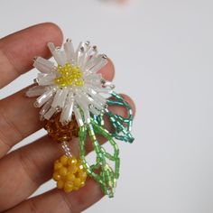 a hand holding a flower brooch with beads on it