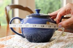 a person measuring the width of a blue teapot