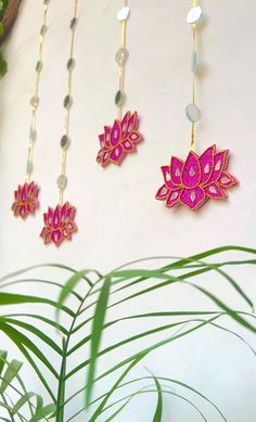 three pink and gold necklaces hanging on a white wall next to a green plant