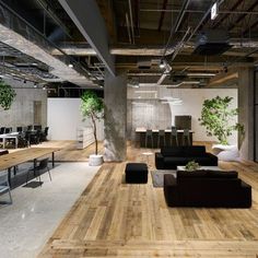 an office with wooden floors and black couches in the center, surrounded by tables and chairs