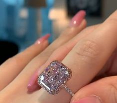 a woman's hand holding an engagement ring with a pink diamond in the center