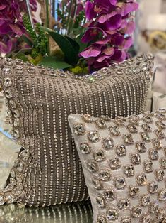 two decorative pillows sitting on top of a table next to a vase with purple flowers