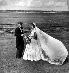 a man and woman standing next to each other in front of a fenced field