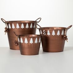 three metal buckets with christmas trees painted on the sides and bows at the handles