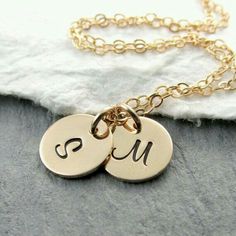 two initial necklaces with the letter s and m in gold on a white cloth