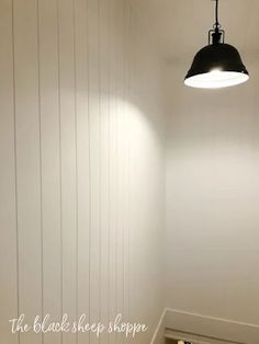 an empty room with white walls and wood flooring is lit by a black pendant light