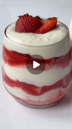 a red and white dessert in a glass with strawberries on top, sitting next to a spoon