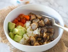 a white bowl filled with rice, meat and veggies next to a fork