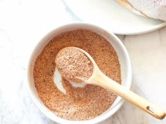 a bowl filled with spices next to a wooden spoon on top of a white counter