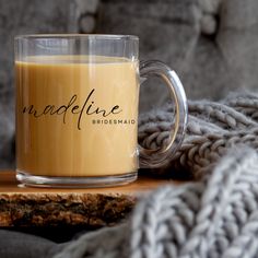 a glass mug sitting on top of a wooden table next to a gray sweater and blanket