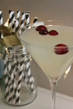 a martini with cherries on the rim and black and white paper straws next to it