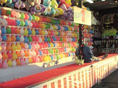 there are many colorful balloons on display at this market stall, and one person is sitting in front of the wall