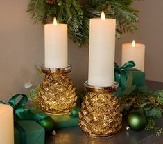 three lit candles sitting on top of a table next to green boxes and christmas decorations