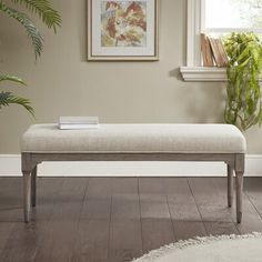 a white bench sitting on top of a hard wood floor next to a potted plant