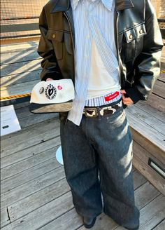 a young man is standing on a deck with his hands in his pockets and wearing a leather jacket