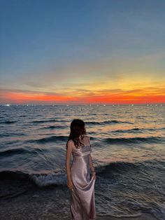 a woman standing on top of a sandy beach next to the ocean at sunset or dawn