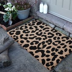 a leopard print door mat sitting on the ground next to a potted plant and flowers