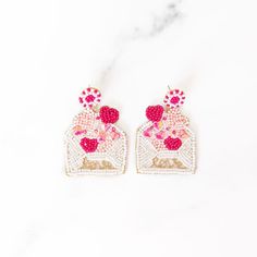 two pairs of pink and white beaded heart shaped earrings on a marble counter top