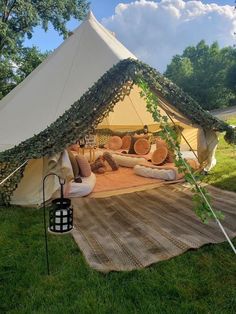 a large tent with pillows and blankets on the ground in a grassy area next to trees