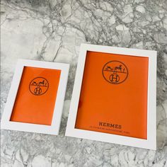 two frames sitting next to each other on a marble counter top with an orange and white border