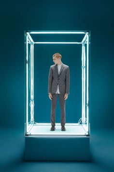 a man standing in front of a glass box with neon lights on the sides and his hands in his pockets