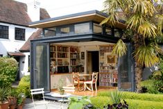 a small house with a table and chairs in front of it, surrounded by greenery