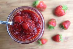 a jar filled with strawberry jam on top of a wooden table next to strawberries