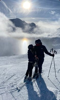 two people on skis standing in the snow with their arms around each other and looking into the distance