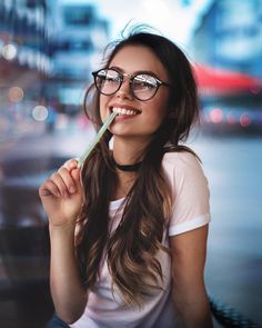 a woman with glasses is holding a toothbrush in her mouth and smiling at the camera