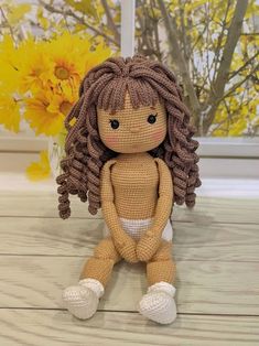 a crocheted doll sitting on top of a wooden floor next to yellow flowers