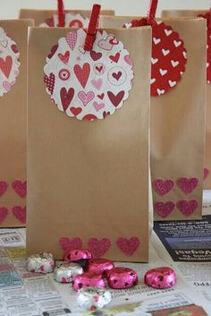 three brown bags with hearts on them sitting on a table next to candy and magazines