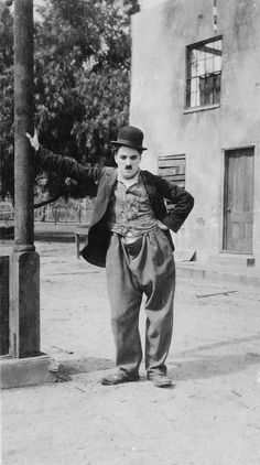 an old black and white photo of a man dressed in clown makeup standing next to a pole