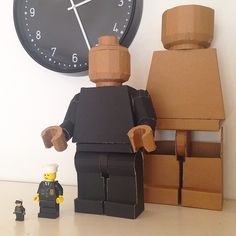 two legos are standing next to a clock and some boxes on the floor,