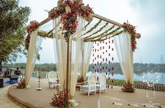 an outdoor wedding setup with white chairs and red flowers on the canopy, decorated with greenery