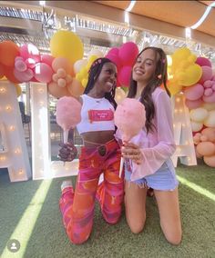 two women sitting on the ground holding lollipops in front of some balloons