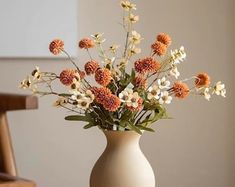 a white vase filled with lots of orange and white flowers on top of a table