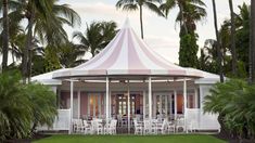 a pink and white tent set up in the middle of palm trees with chairs around it