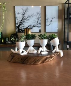 three white ceramic planters sitting on top of a wooden table in front of paintings