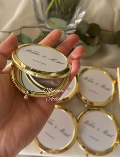 a person holding a compact mirror in front of some other small round mirrors with names on them