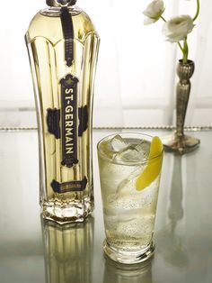 a bottle and glass sitting on top of a table next to a vase with flowers