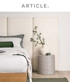 a white bed sitting next to a vase with flowers in it on top of a wooden table