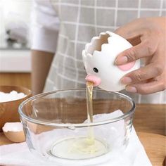 a person pouring liquid into a bowl with an egg shell in it on a wooden table