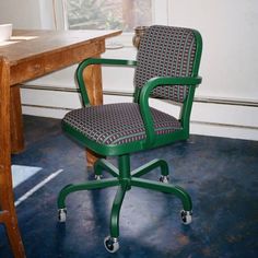 a green office chair sitting in front of a wooden table with a cup on it